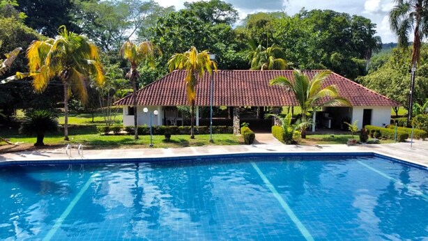 A swimming pool with a tiled deck, a building with a red-tiled roof, and surrounding greenery.