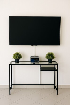 Ein modernes Zimmer mit einem großen Flachbildfernseher an der Wand, einem Glastisch mit zwei Topfpflanzen und einem kleinen Radio.