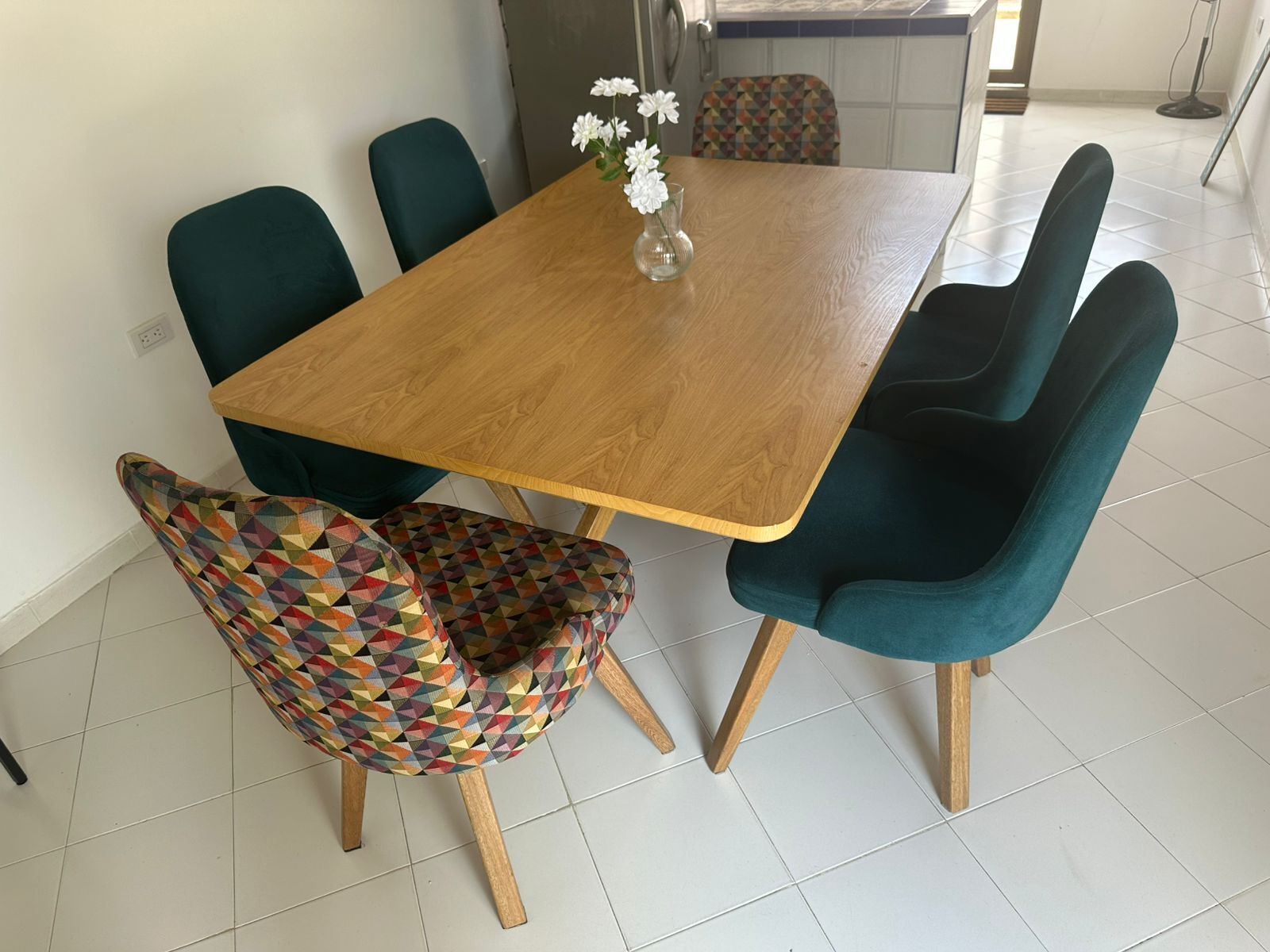 A dining table with a vase of flowers, surrounded by chairs.