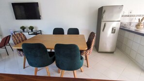 Un comedor con una mesa y sillas de madera, un televisor montado en la pared y un refrigerador en la cocina.