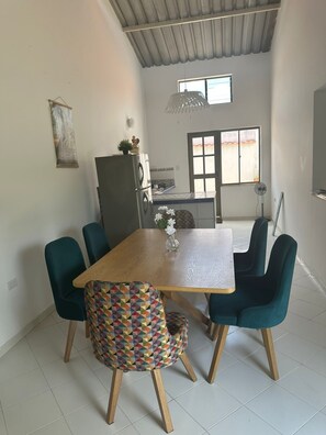 A dining area with a wooden table and teal chairs, a refrigerator, and a window with a view.