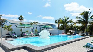Une piscine agrémentée d’une fontaine en forme de coquillage, de chaises longues et de parasols.