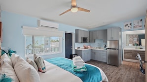Une chambre à coucher moderne avec un lit, un ventilateur de plafond et une vue sur la cuisine.