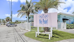 Une enseigne indiquant « The Pearl Cabana Club », avec une clôture blanche et des palmiers.