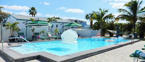 A swimming pool with a shell-shaped fountain, lounge chairs, and umbrellas.