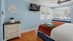 A bedroom with a bed, a TV, a dresser, a window with blinds, and a ceiling fan. - Unit 112 Studio King Suite - The Pearl Cabana Club (St Pete Beach)