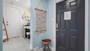 A hallway with a white door, a dark door with a notice, a wall hanging, and a small wooden stool. - Unit 112 Studio King Suite - The Pearl Cabana Club (St Pete Beach)
