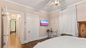Et soveværelse med seng, ventilator, fjernsyn, vækkeur og en dør til et andet rum.
