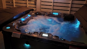 A hot tub with blue lighting, surrounded by wooden slats and a sign with hot tub rules.