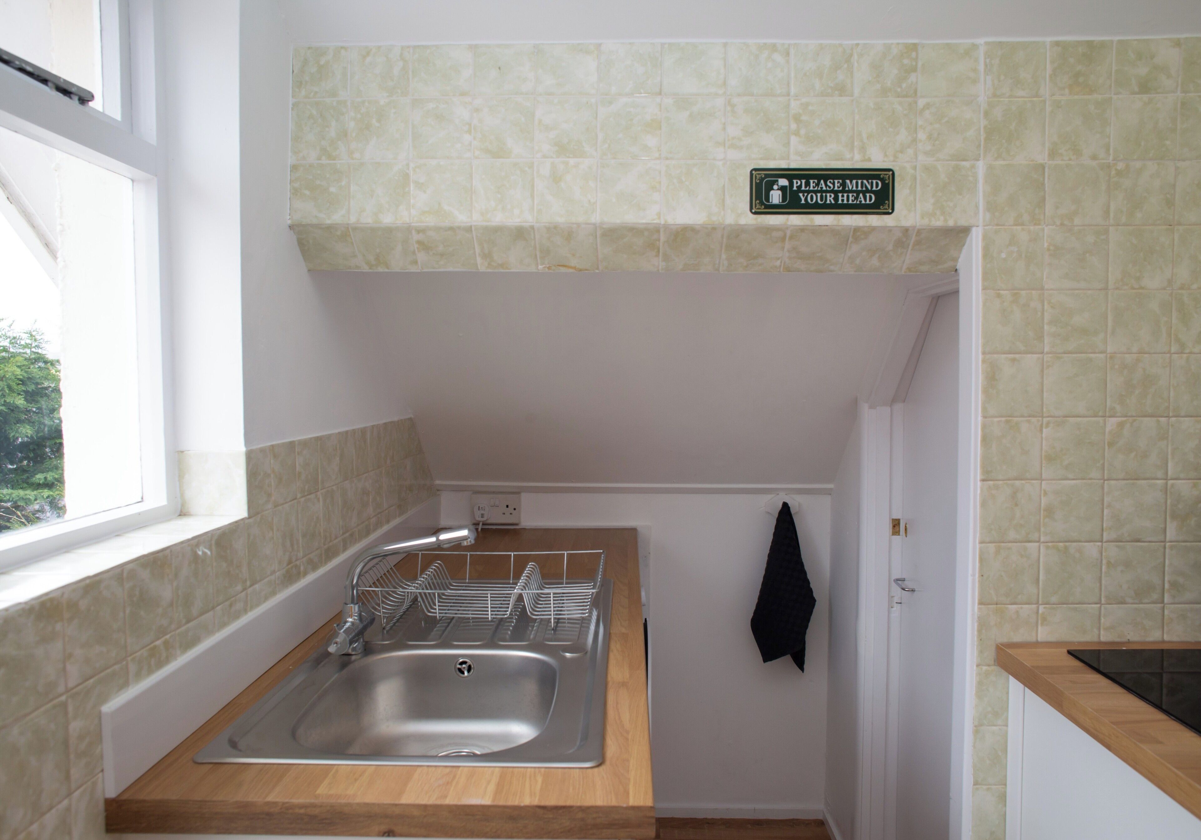A small kitchen with a sink, a window, and a sign on the wall.