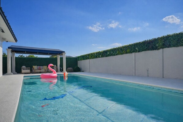 A swimming pool with a pink flamingo float, a blue fish float, and a beach ball. - Pearl Luxury Oasis · Heated Pool · Game Room (Miami)