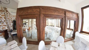 Un espace repas avec des tables rondes, des chaises blanches et un grand buffet en bois orné de sculptures complexes.
