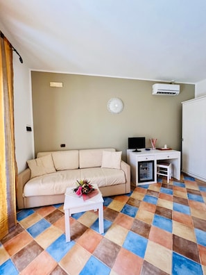 Una sala de estar con un sofá, una mesita con un adorno, un televisor y un escritorio con una silla.