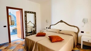 Une chambre avec un sol à carreaux, deux lits avec des têtes de lit assorties, un miroir, des lampes de chevet et une porte donnant sur une salle de bain.