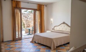 Una camera da letto con un letto, un comodino, una lampada a parete e vista su uno spazio esterno con un muro in pietra e un tavolo.