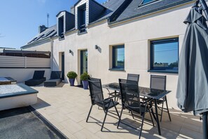 Een moderne patio met een glazen tafel en stoelen, potplanten en een overdekte zithoek.