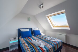Een slaapkamer met dakraam, een bed met blauwe kussens, een nachtkastje met telefoon en een radiator.