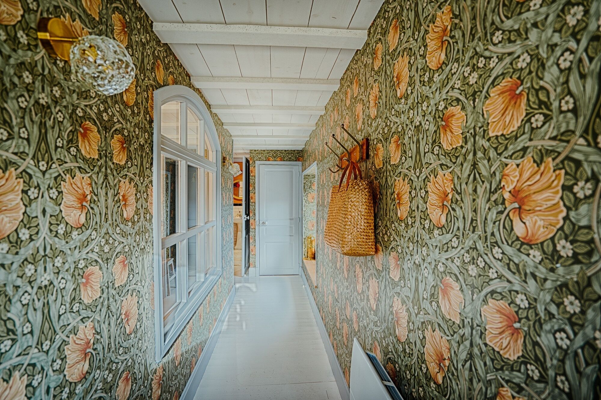 A hallway with floral wallpaper, a white door, and a hanging basket.