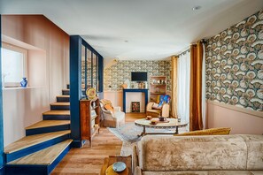 Un salon avec un escalier, une cheminée et un papier peint à motifs.