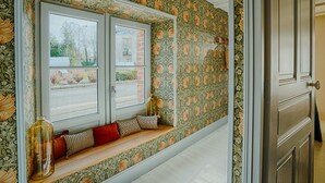 Um quarto com janela, um banco com almofadas e papel de parede floral.