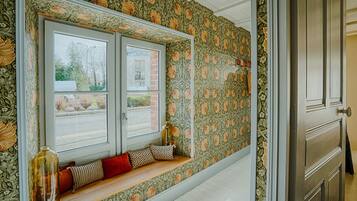 Une pièce avec une fenêtre, un banc agrémenté de coussins et un papier peint à motifs floraux.