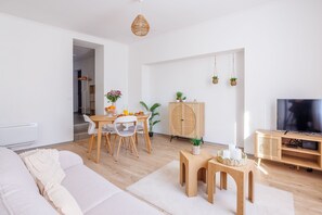Moderni olohuone, jossa on sohva, ruokapöytä, tuoleja, televisio ja kaappi.