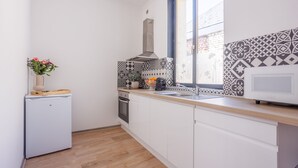 Een keuken met witte kastjes, een magnetron, een fornuis en een raam met patroon tegels.