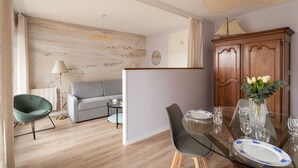 A modern living room with a sofa, a dining table set for two, and a wooden cabinet. - Le Doux Rivage - 100 m de la plage (Dinard)