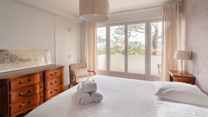 A hotel room with a bed, a wooden dresser, a chair, a lamp, and a large window with curtains. - Le Doux Rivage - 100 m de la plage (Dinard)
