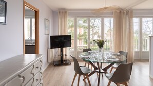 A modern dining area with a glass table, chairs, and a TV. - Le Doux Rivage - 100 m de la plage (Dinard)