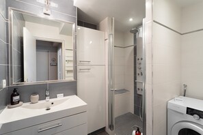 A modern bathroom with a large mirror, a sink, a shower, and a washing machine. - Le Doux Rivage - 100 m de la plage (Dinard)