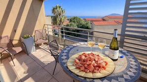 Ein Balkon mit Tisch, Stühlen, einer Weinflasche und einer Platte Wurstwaren.