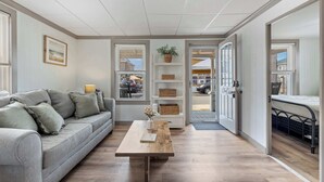 Ett modernt vardagsrum med en soffa, ett soffbord i trä och utsikt genom en öppen dörr ut mot omvärlden.