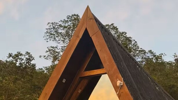 Eine moderne Holzhütte mit einem Satteldach, großen Glasfenstern und Korbmöbeln auf einer Außenterrasse.
