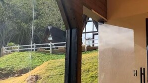 Ein Zimmer mit großem Fenster, Holzboden und Blick auf einen grasbewachsenen Hügel und einen weißen Zaun.