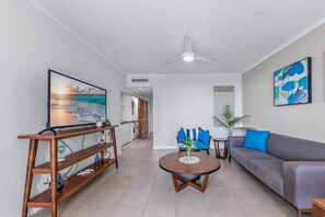 A living room with a TV, sofa, coffee table, and artwork. - Ocean Rise at Airlie One (Airlie Beach)