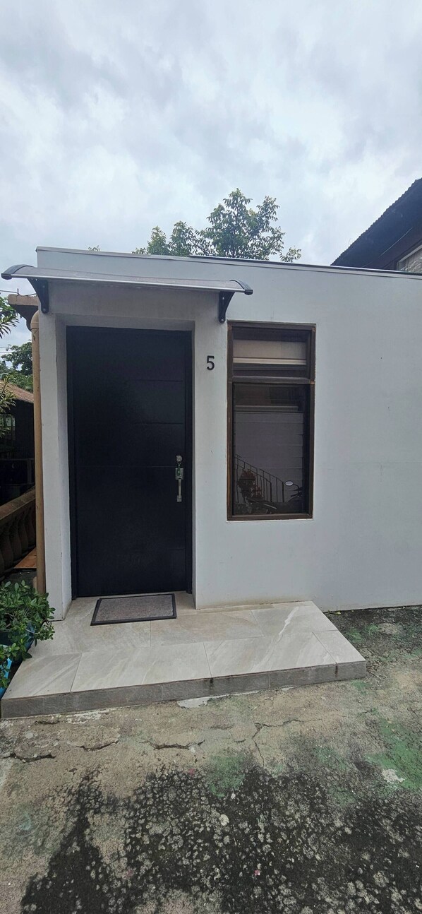 Un petit bâtiment d’un seul étage, avec une porte noire et une fenêtre sur le côté droit.