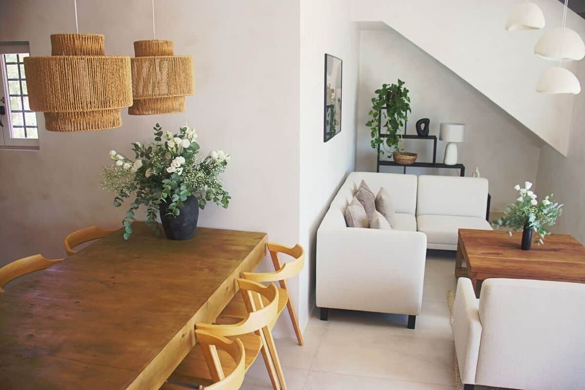A dining area with a wooden table and chairs, a white sofa, and hanging wicker lamps.