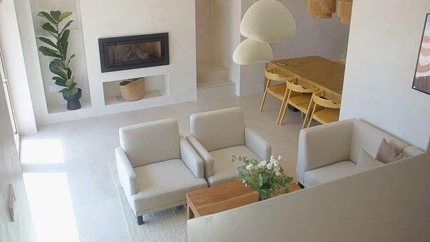 A modern living room with a sofa set, a dining table with chairs, a fireplace, and pendant lighting.