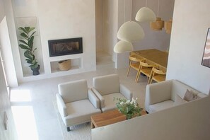 A modern living room with a sofa set, a dining table with chairs, a fireplace, and pendant lighting.