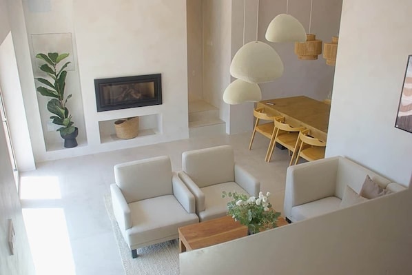 Una sala de estar moderna con un conjunto de sofás, una mesa de comedor con sillas, una chimenea e iluminación colgante.