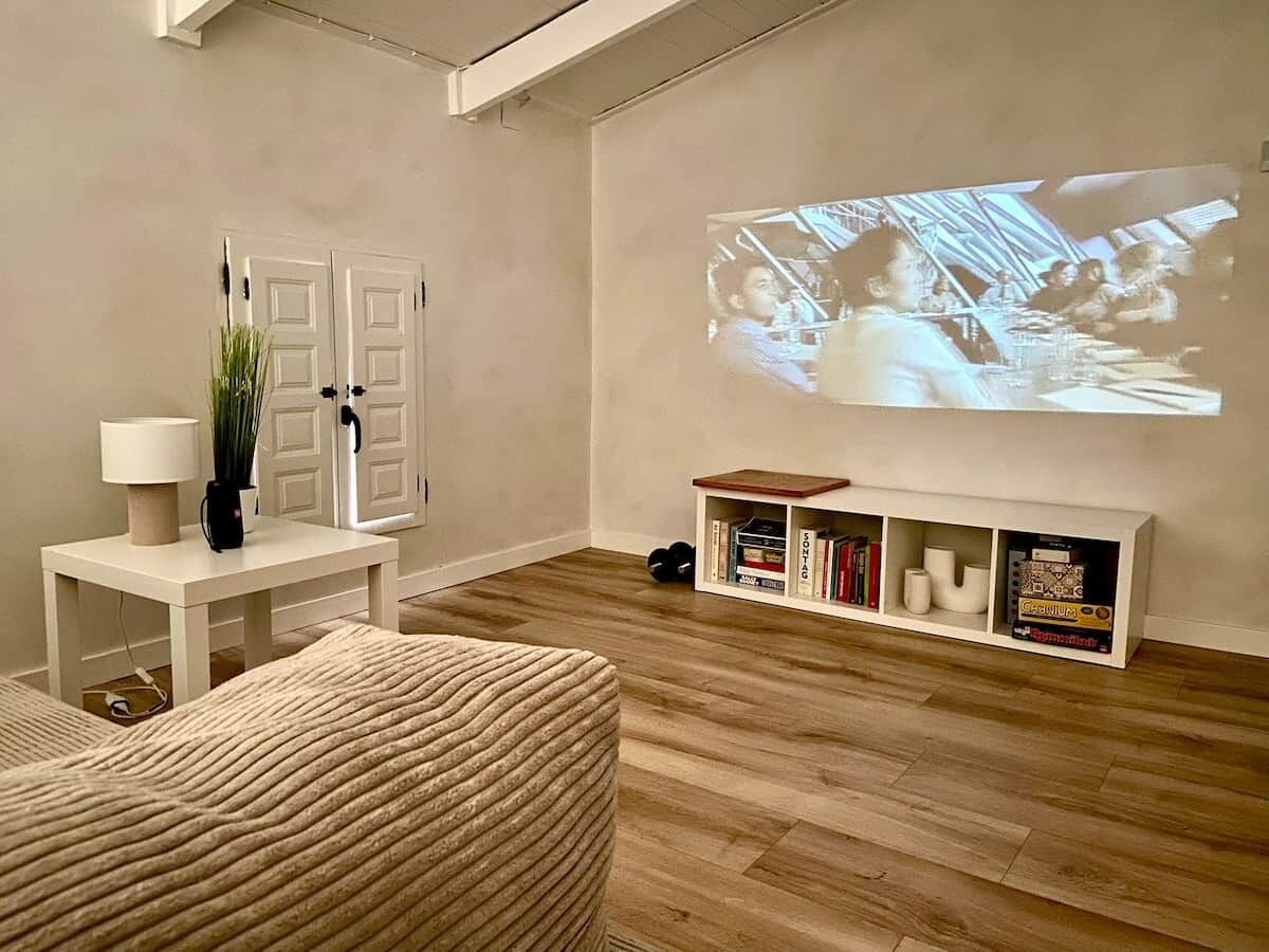 Un saló amb pantalla de projector, una biblioteca blanca i un otomà estampat.