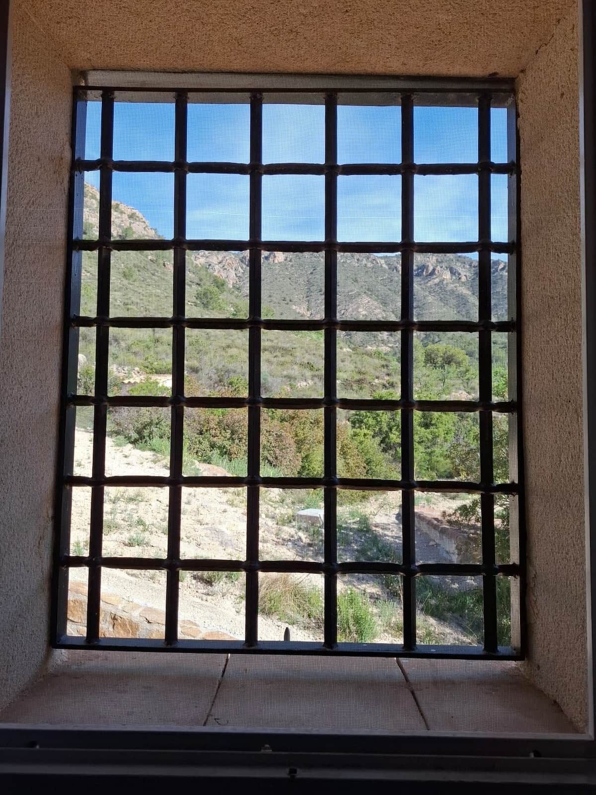 Una ventana con un diseño de cuadrícula, con vistas a un paisaje natural de colinas y vegetación escasa.
