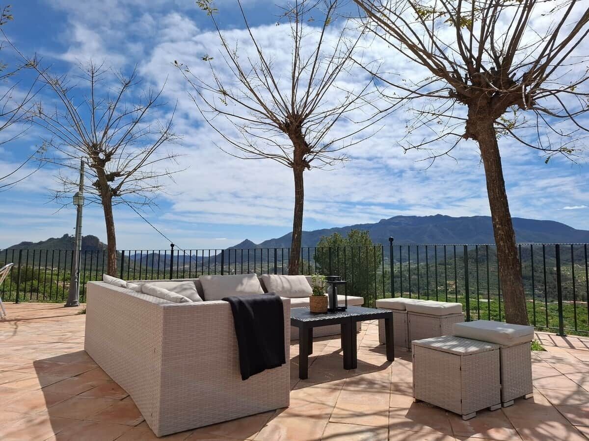 An outdoor seating area with a sofa, armchairs, and a table, overlooking a mountainous landscape.