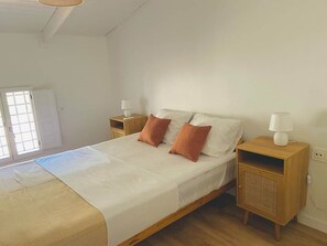 A single-bed room with a wooden headboard, two bedside tables with lamps, a window with blinds, and a door.