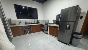 Een keuken met een grote, roestvrijstalen koelkast, houten kasten, een betegelde vloer en een flatscreen televisie die boven de aanrecht is bevestigd.
