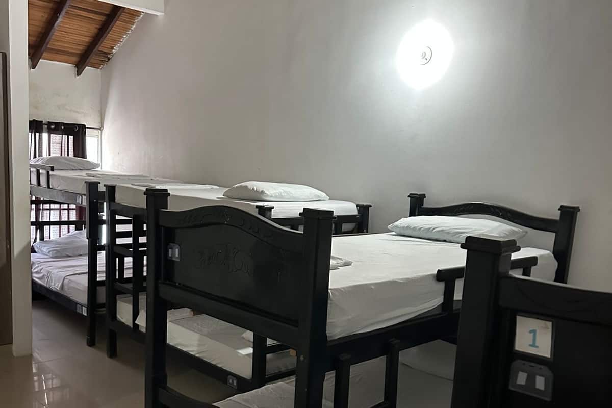 Une chambre de dortoir avec des lits superposés, un ventilateur de plafond et un luminaire.