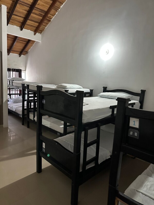 Une chambre de dortoir avec des lits superposés, un ventilateur de plafond et un luminaire.