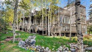 A modern building with a wooden deck, surrounded by birch trees and a garden with yellow flowers. - Sonnenblick by Snowmass Vacations (Snowmass Village)
