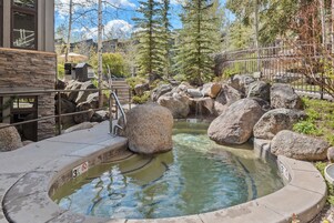 Un área de aguas termales con rocas grandes, una terraza de madera y un edificio de piedra con fachada de piedra.